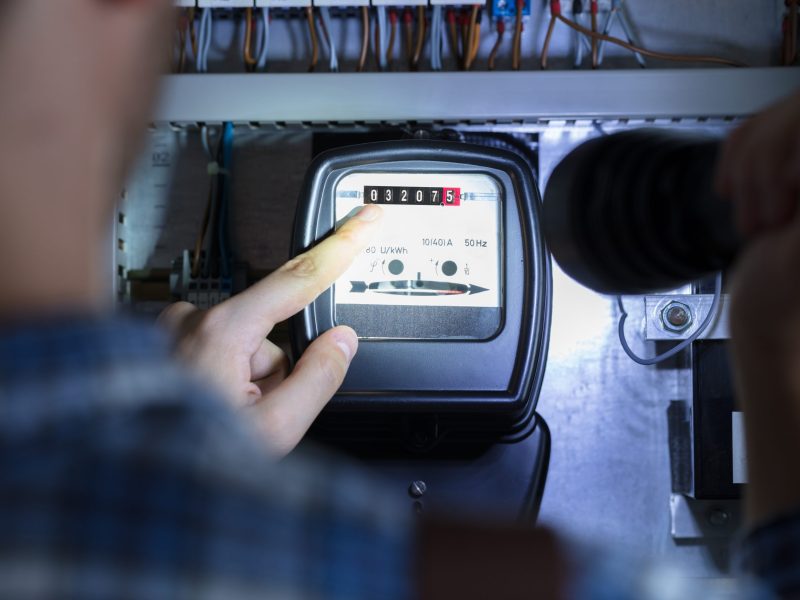 Person's Finger Pointing To Electric Meter Reading Using Flash Light